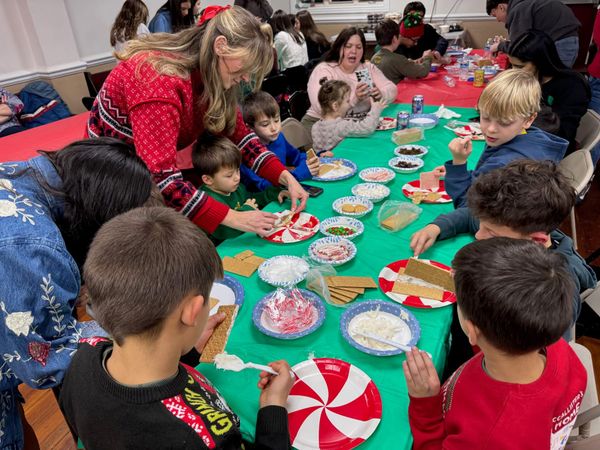 Children gathered around a festive table decorating Christmas treats with a teacher