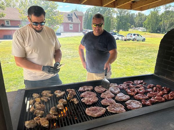 Two men grilling meat under the pavilion